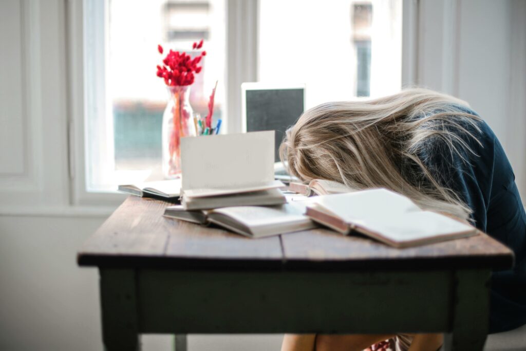 woman with head on her desk, surrounded by books