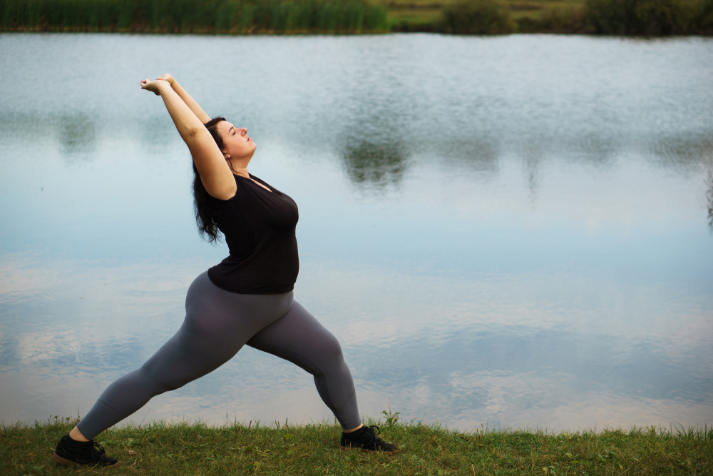Overweight woman training near lake, copy space. Healthy lifestyle, sport, weight losing, activity concept

