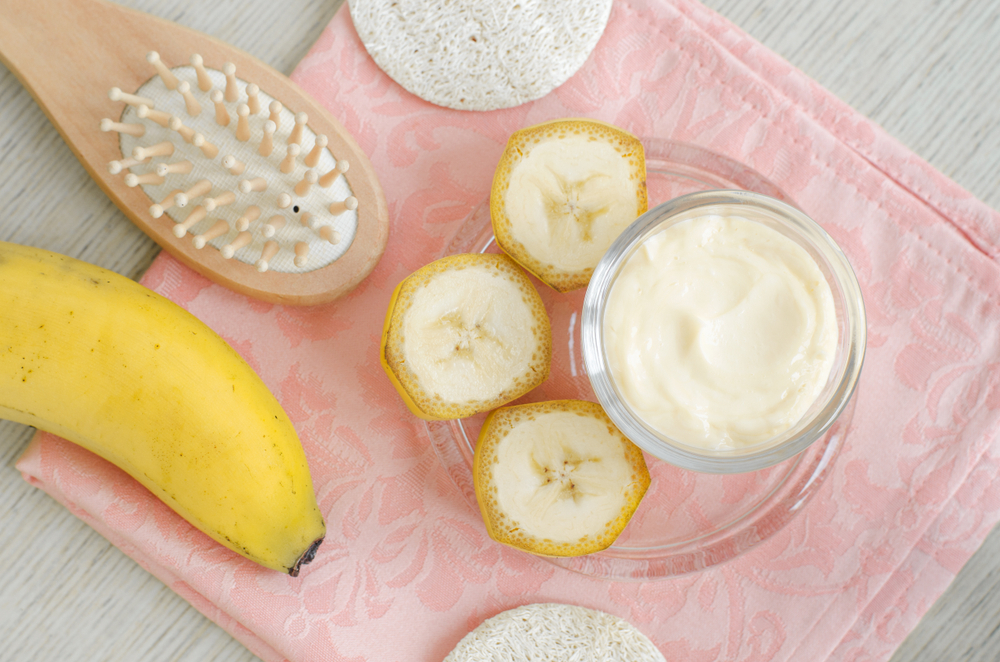 Homemade banana face and hair mask (cream) in the small glass jar and wooden hair brush. DIY beauty treatments and spa. Top view, copy space.
