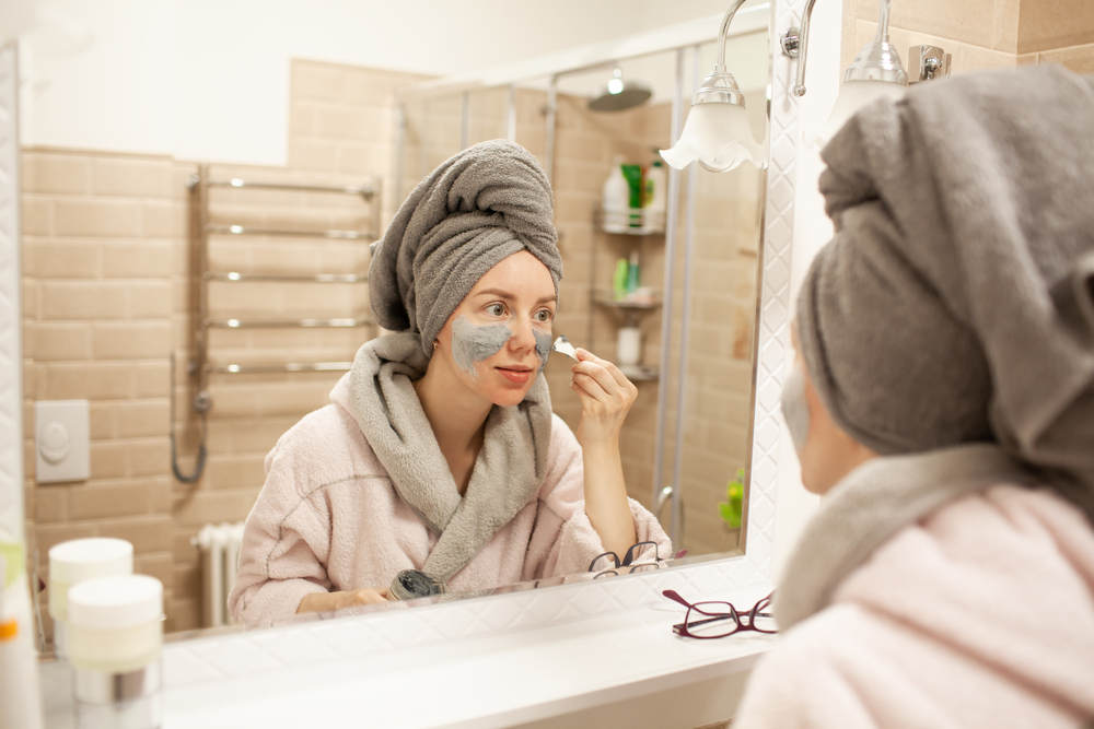 Face mask foam bubbles charcoal detox facial treatment at home -asian girl purifying skin removing dead skin cells with chemical peel korean face sheet in bathroom.
