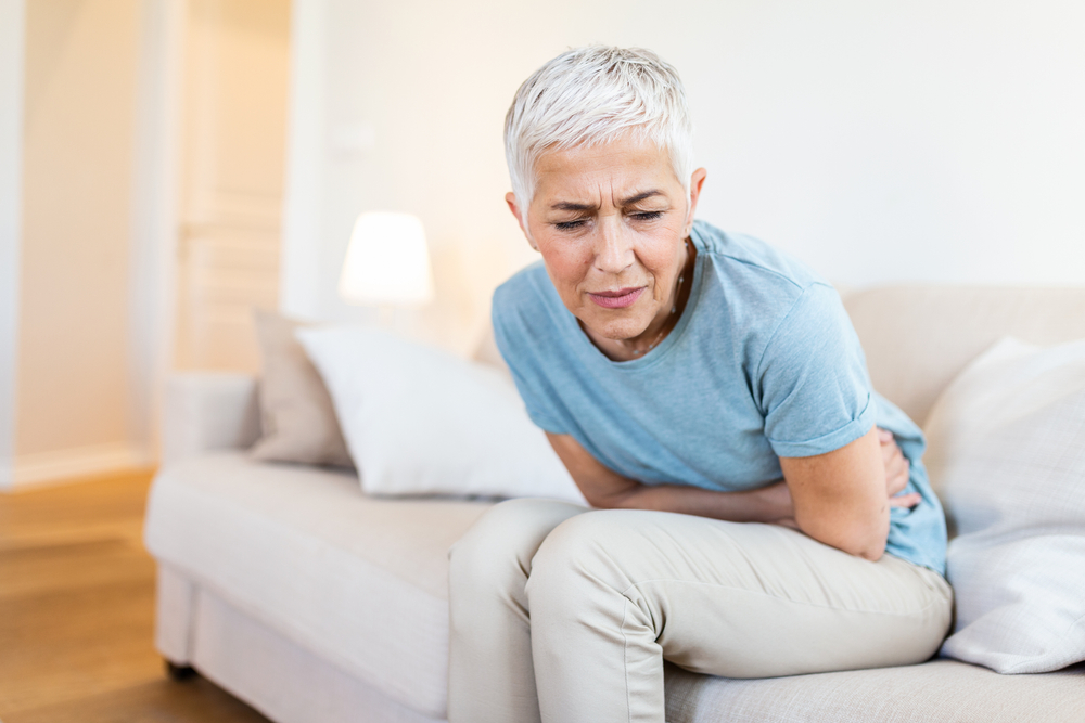 Middle-aged woman sitting on bed feels unhealthy touch stomach suffers from severe crampy abdominal pain,
