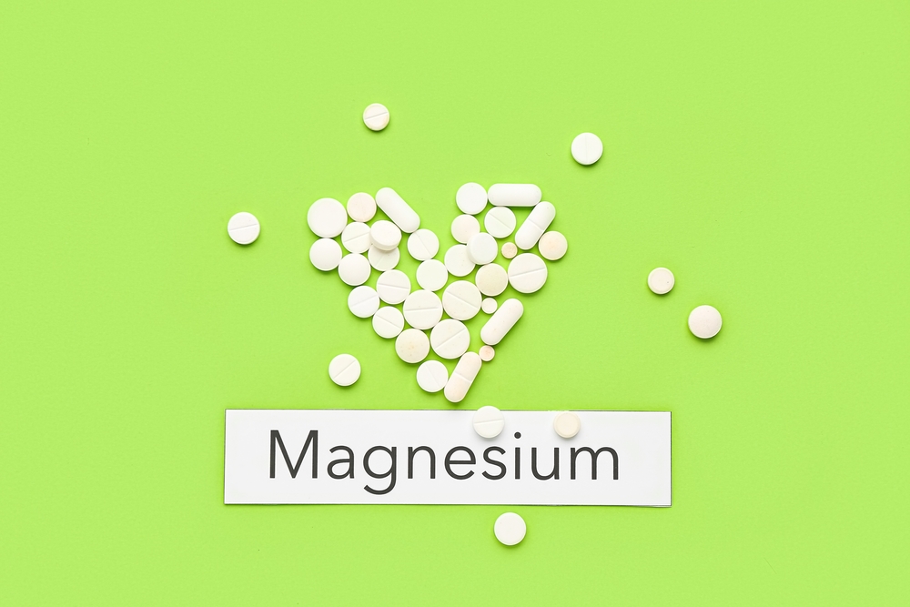 Heart made of pills and word Magnesium on green background