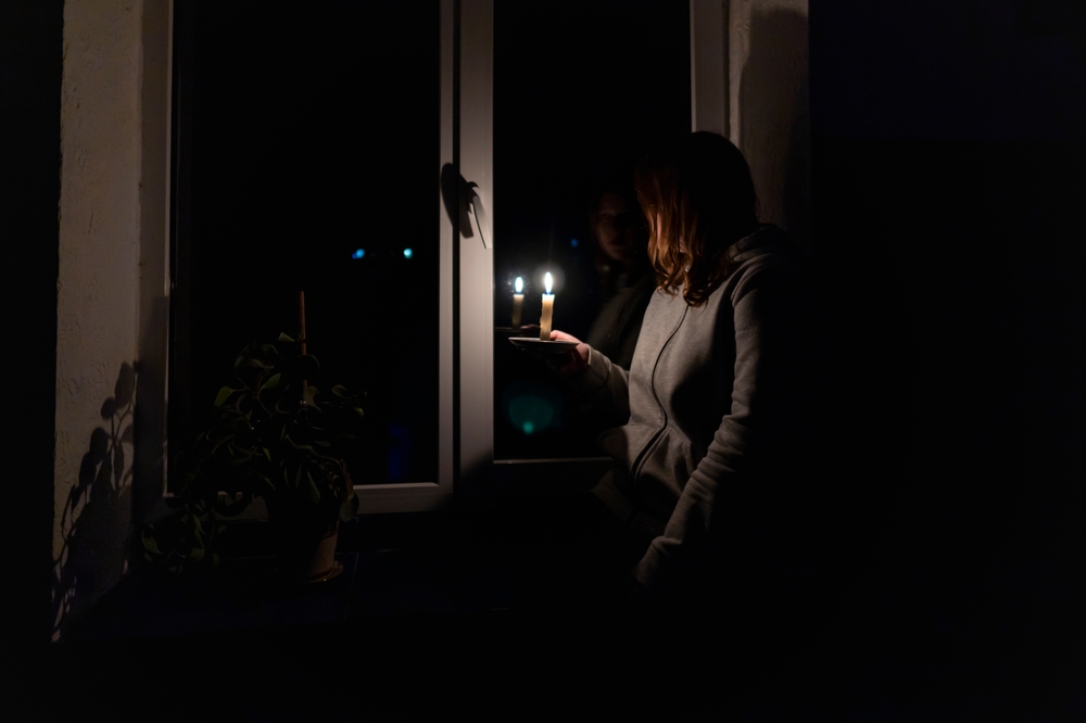 Blackout. Energy crisis. Destruction of infrastructure. Power outage concept. Girl with a burning candle in a dark room sits near the window
