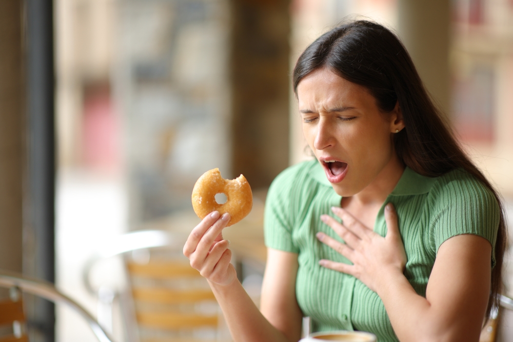 Stressed woman choking eating doughnut in a bar terrace
