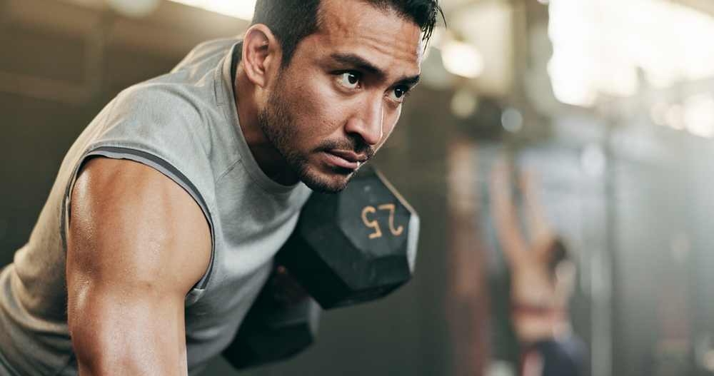 Serious man, dumbbell and weightlifting in workout, exercise or fitness at indoor gym. Active male person, bodybuilder or athlete lifting weight for intense arm training, strength or muscle at club
