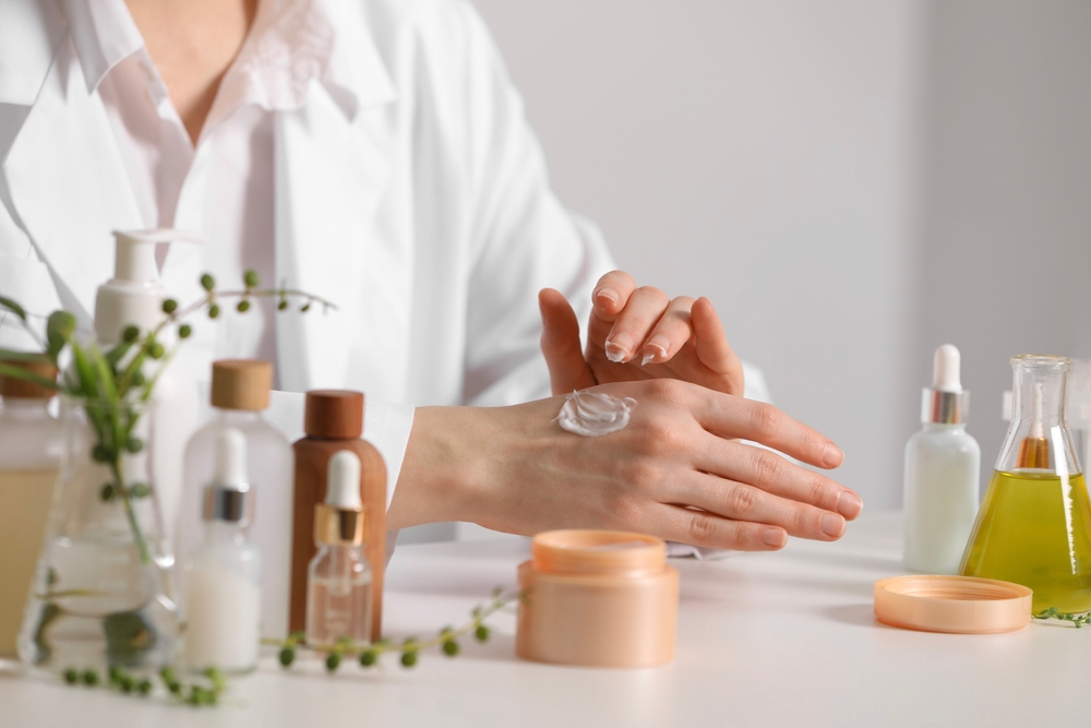 Dermatologist applying cream onto hand at white table indoors, closeup. Testing cosmetic product
