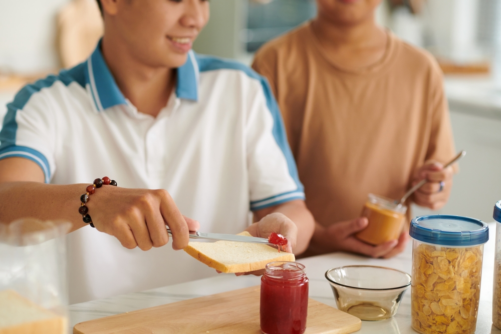 Cropped image of father making peanut butter jam sandwiches for son