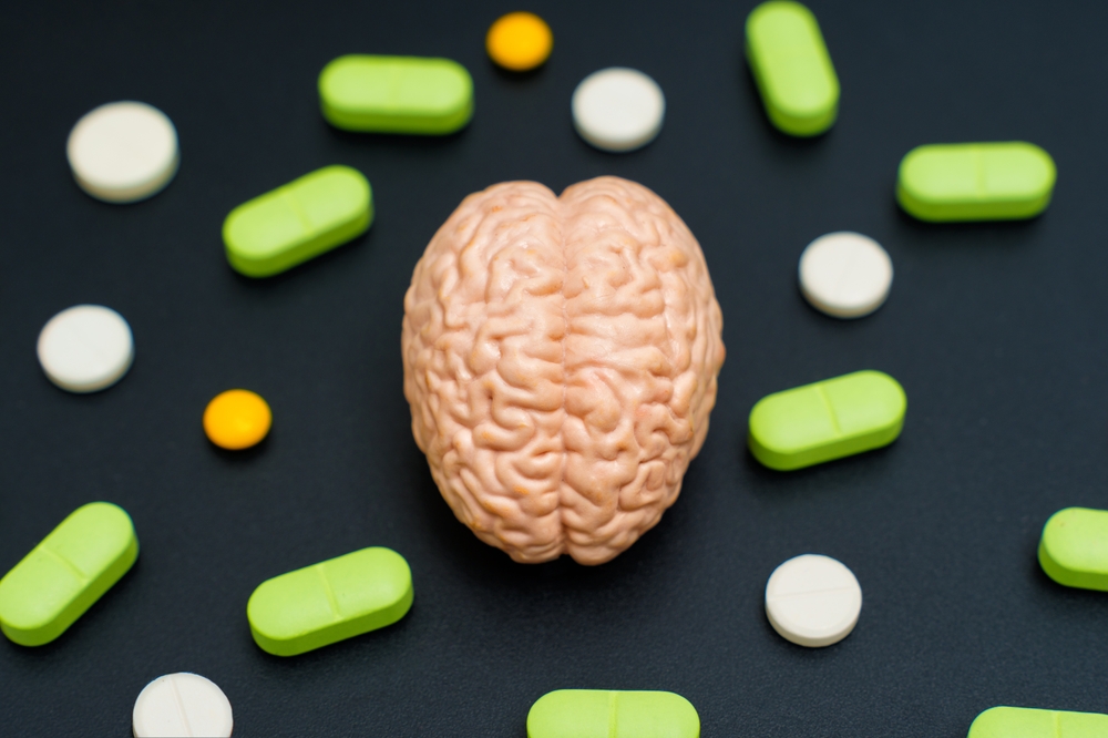 Clay brain model surrounded by variously colored pills on a black surface. Mental health, medical treatment, neuroscience, and pharmacology concept.