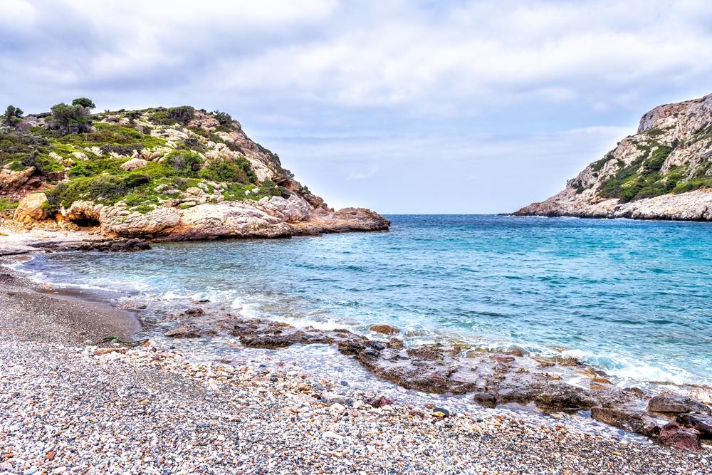 Iero beach on Ikaria island, Greece cove with Ikarian sea waves washing on coast shore rocks by Dionysos cave temple in summer
