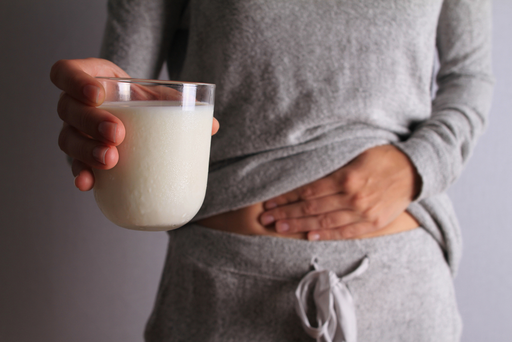 Woman with stomach pain holding a glass of milk. Dairy Intolerant person. Lactose intolerance, health care concept.
