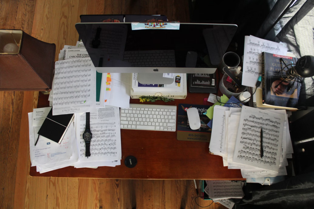 A cluttered desk featuring a computer, keyboard, mouse, lamp, and scattered papers, embodying a creative workspace.