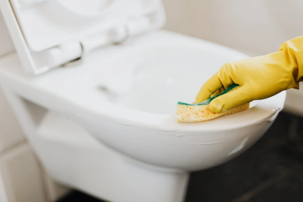 A person wearing yellow gloves diligently cleans a toilet, emphasizing hygiene amid chemotherapy and infection risk concerns.