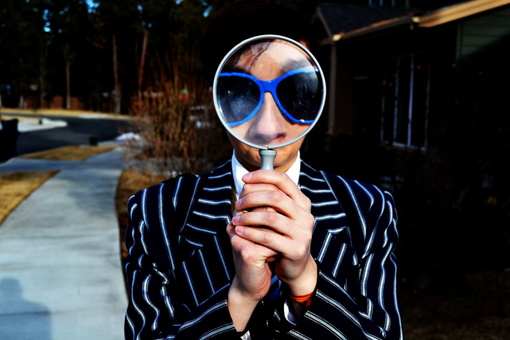 A person in a striped suit holding a magnifying glass over their face, symbolizing the scrutiny of deceptive practices.