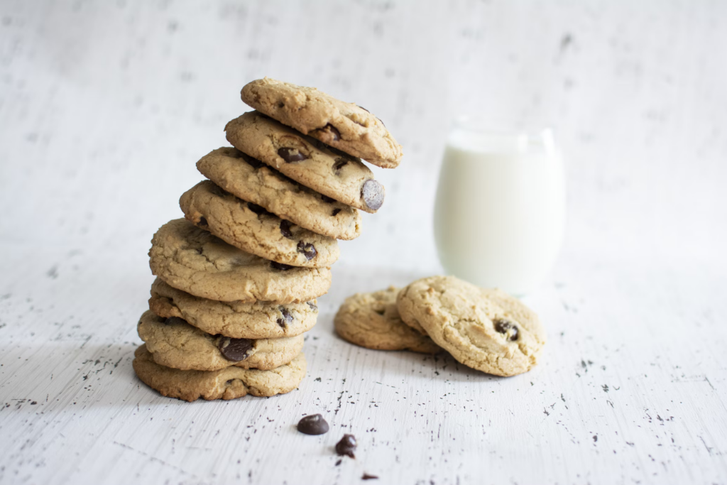 A stack of chocolate chip cookies on a wooden table beside a glass of milk, highlighting a tempting yet inflammatory treat.