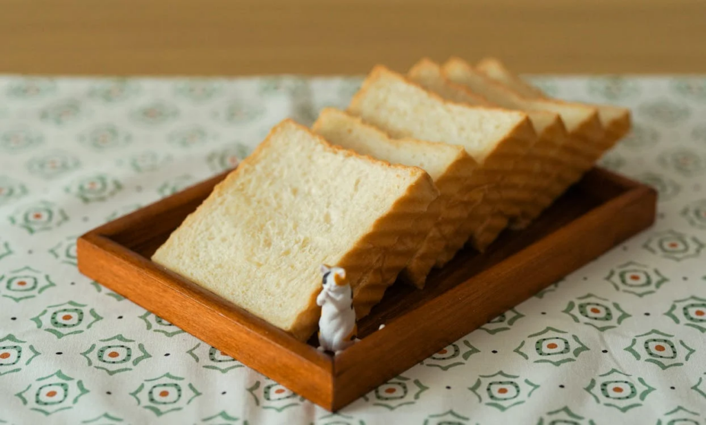 Sliced white bread arranged in a wooden tray, placed on a table, highlighting its comforting yet joint-unfriendly nature.
