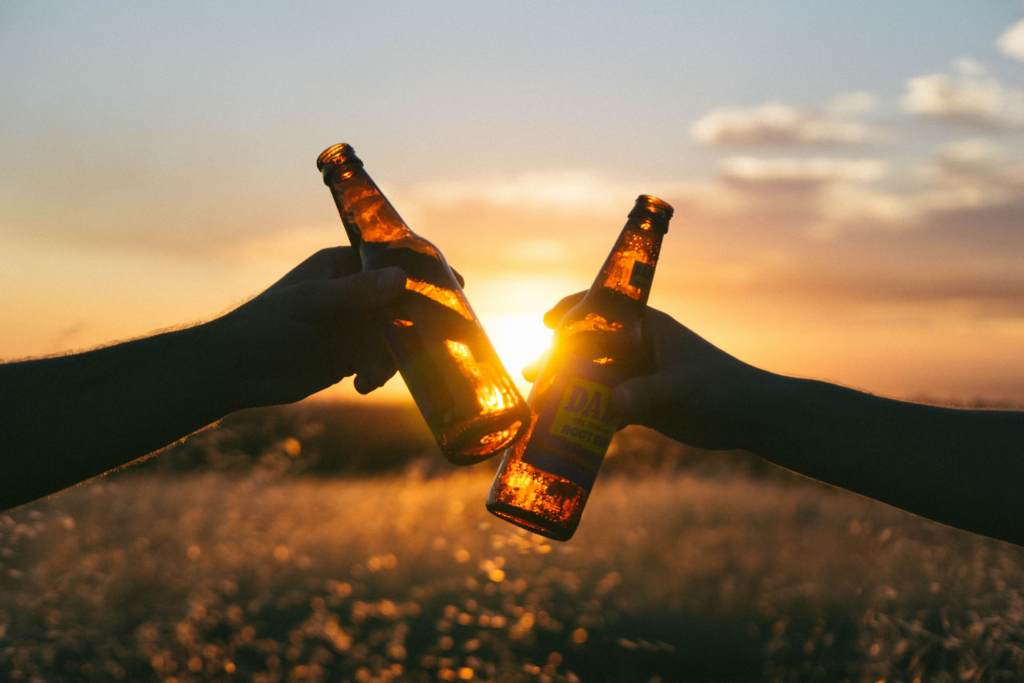 Two people raise beer bottles against the sun, reminding viewers of the health implications of excessive alcohol consumption.