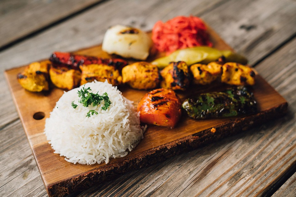 A wooden cutting board adorned with Mediterranean cuisine, including colorful vegetables and fluffy rice.