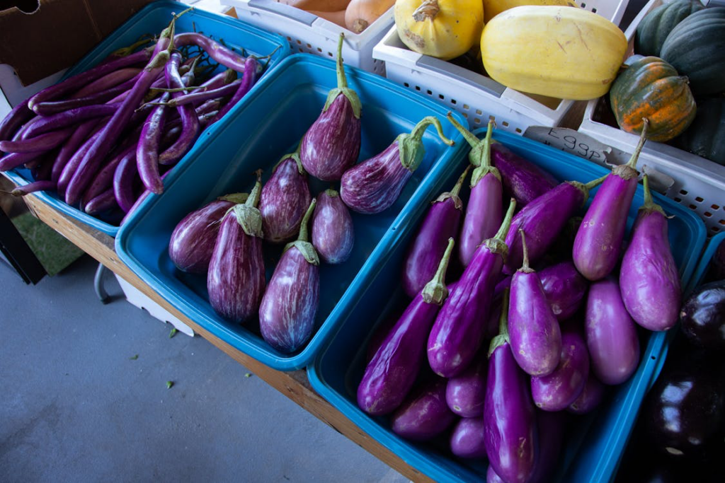 Display of purple eggplants alongside other vegetables in blue containers, highlighting a vibrant selection of fresh produce, which is one of the worst foods for arthritis