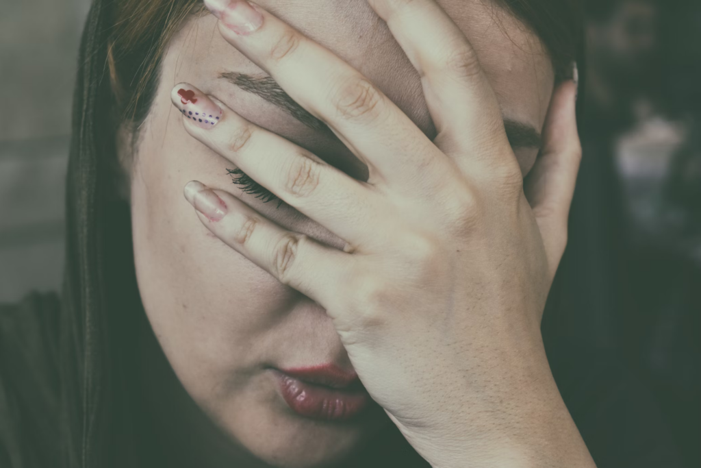 A person holding their hand over their face, with fingers pressing against the forehead and temple area. This gesture is commonly associated with someone experiencing a headache or migraine. The individual's expression appears to convey discomfort or pain, further suggesting that they are dealing with head-related discomfort. The close-up nature of the photo emphasizes the intensity of the sensation being felt.