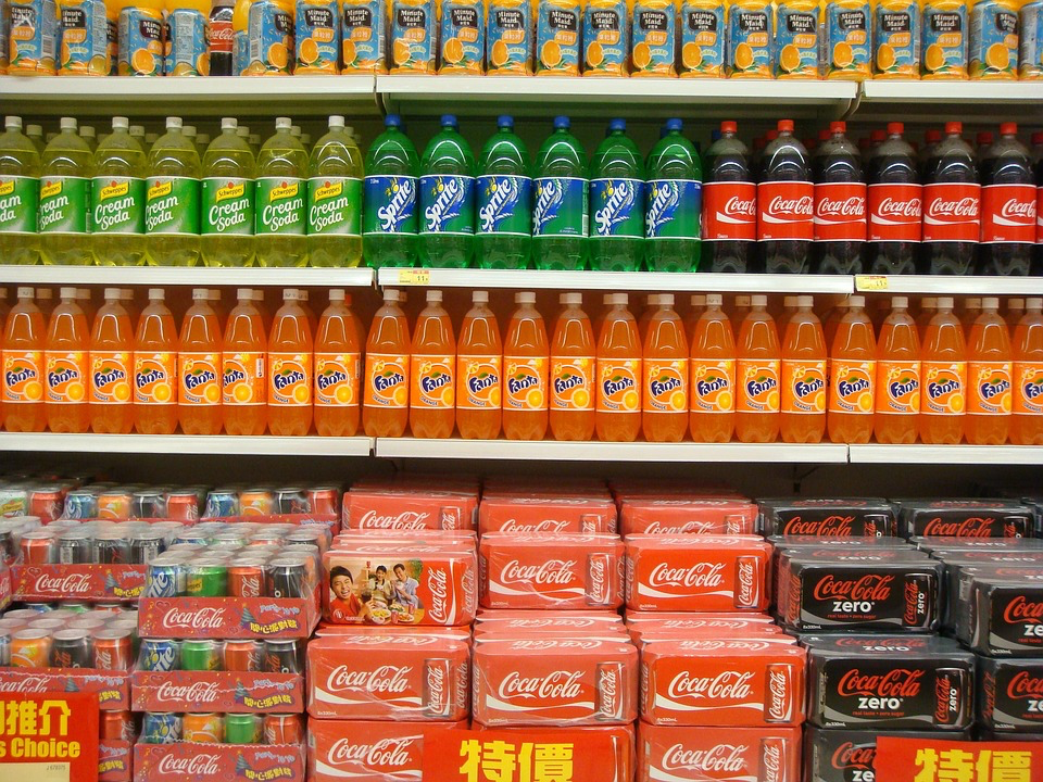 A supermarket shelf stocked with various soft drinks, including brands like Coca-Cola, Fanta, Sprite, and cream soda, highlighting the context of soft drinks and bone health.