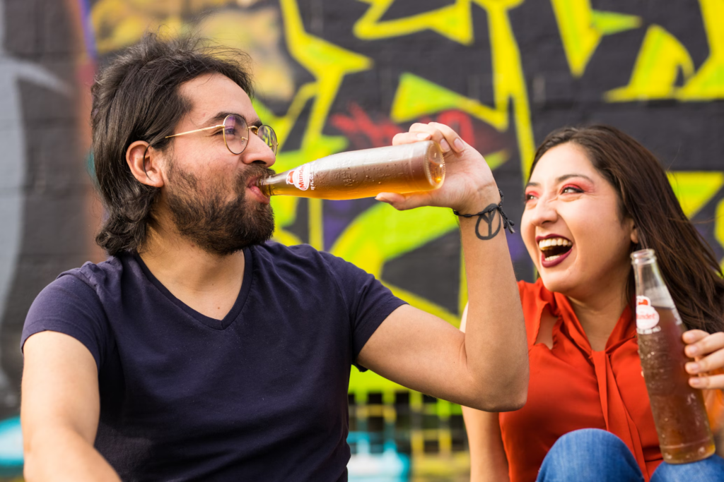 The image shows two individuals enjoying a casual moment while drinking beverages, highlighting the social and cultural aspects of consuming soft drinks.