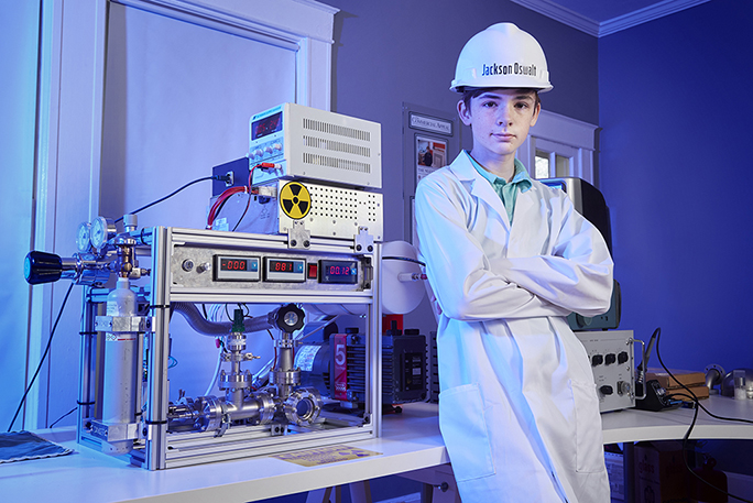 Jackson Oswalt seen wearing a lab coat and safety helmet posing with his project on nuclear fusion.
