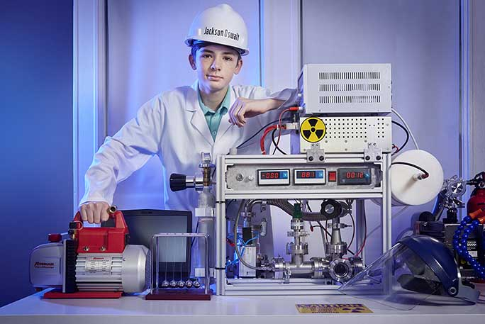 Jackson Oswalt seen wearing a lab coat and safety helmet posing with his project on nuclear fusion.
