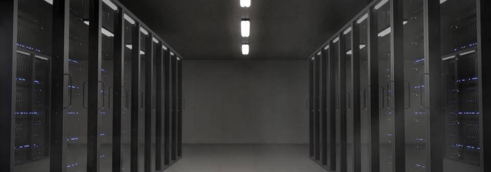 Dark server room with rows of data center cabinets featuring blue indicator lights, representing the cloud infrastructure where voice recordings from Echo devices will be processed after March 28.