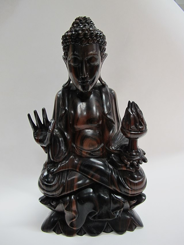 Dark wooden Buddha statue with hands in mudra positions. This detailed carving shows Buddha in traditional meditation posture with distinctive hand gestures that reflect spiritual teachings.
