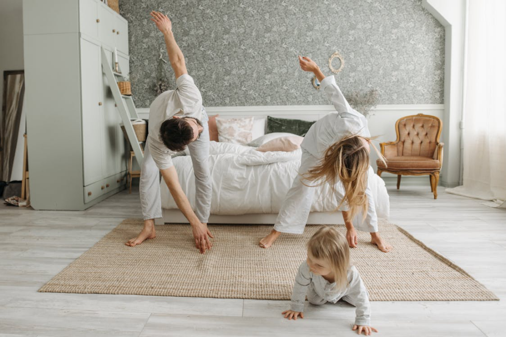 Family practicing yoga together at home. A parent, child, and adult in white clothing perform yoga poses on a natural fiber mat in a bright, minimalist bedroom with natural light.