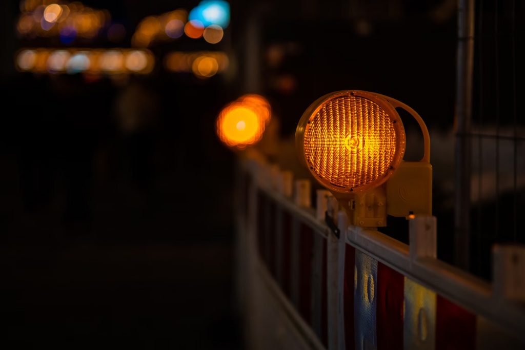 Construction warning light glowing orange against a dark background. The focused light creates a bokeh effect with other lights blurred in the distance.