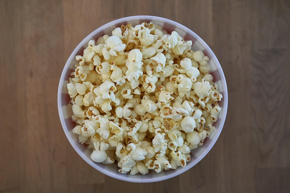 Fresh, fluffy white popcorn in a white ceramic bowl, photographed from above with a wooden background.