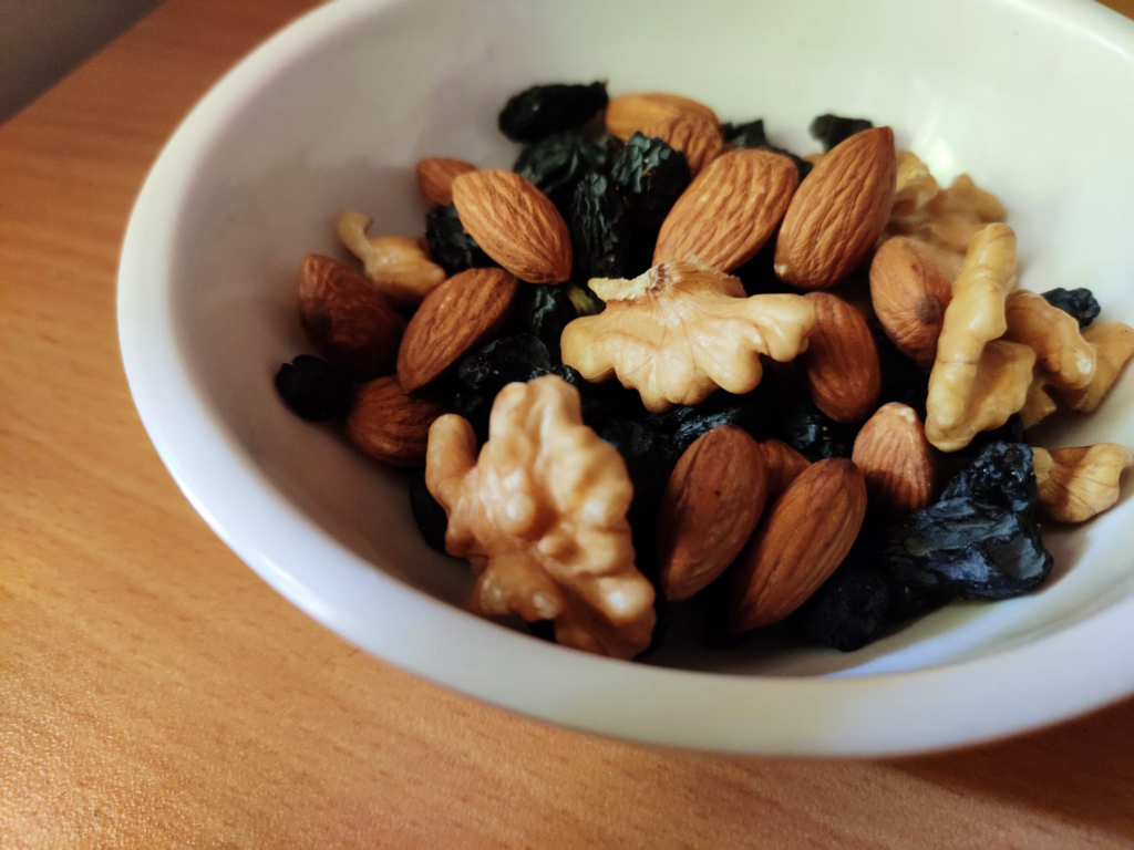 Healthiest snacks featuring a mix of almonds, walnuts, and dark raisins in a white ceramic bowl, showcasing a nutritious and balanced snack option.