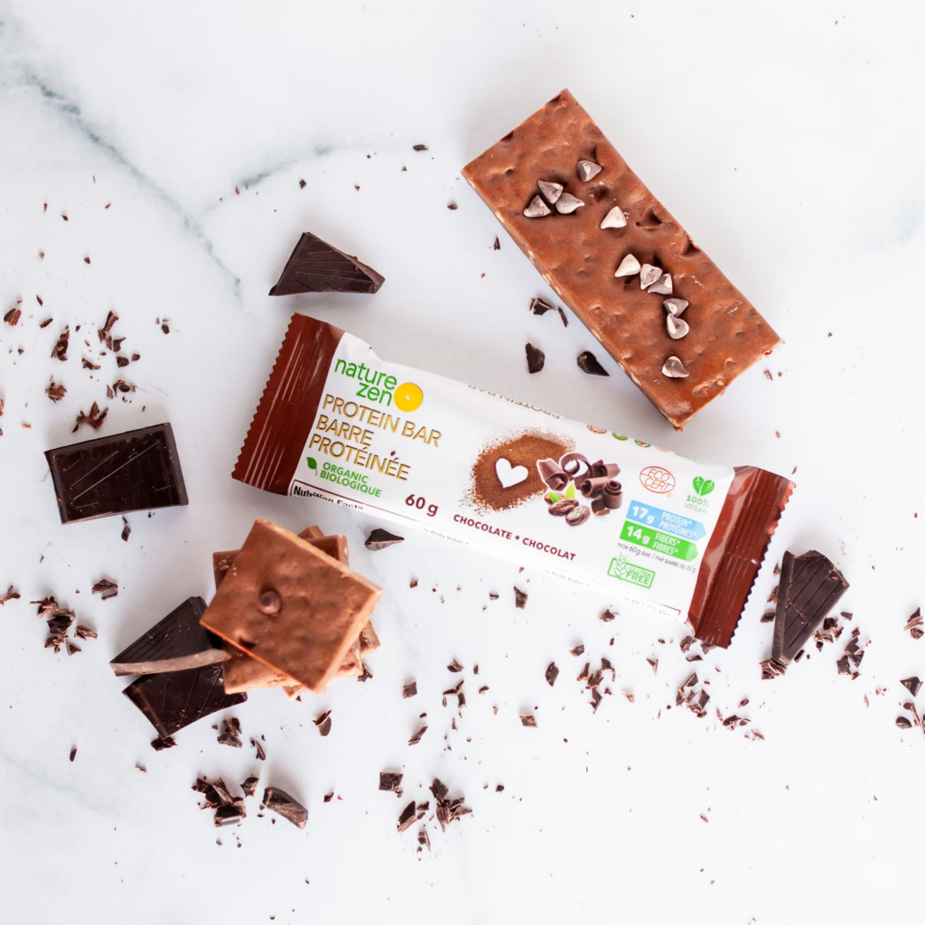 Nature Zen chocolate protein bars scattered on a marble surface with chocolate pieces and crumbs, highlighting a protein-rich snack.