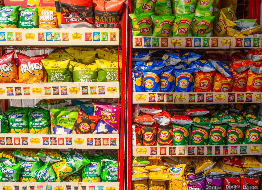 Shelves stocked with various chip brands including Lay's, Kurkure, and other snack packages in a convenience store or supermarket setting.