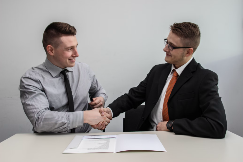 Two professionals shaking hands during a job interview, with documents on a table in front of them.