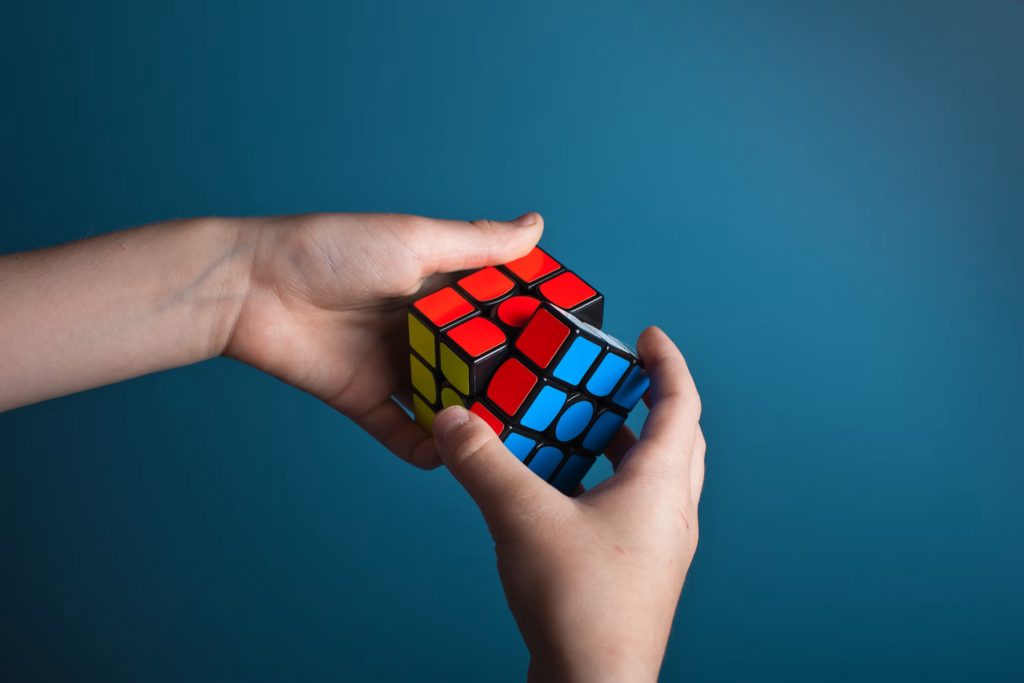 Hands solving a colorful Rubik's cube against a blue background, demonstrating problem-solving skills assessed in job interview questions.