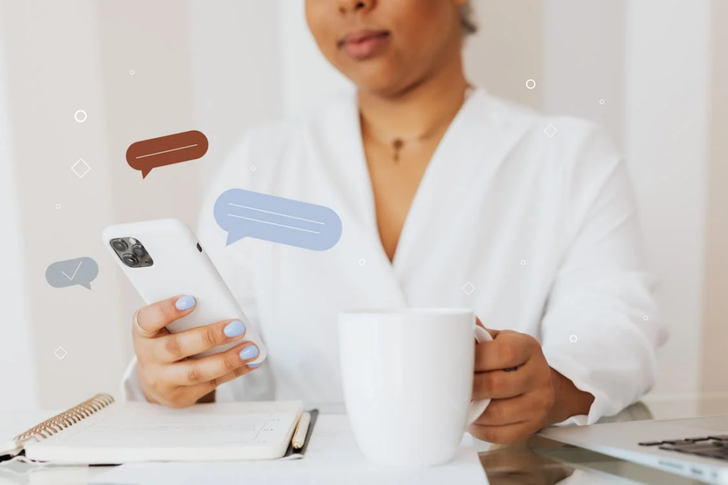 A woman in a white robe holding a smartphone and coffee mug at a desk. The image shows just her torso and hands with light blue nail polish. Animated chat bubble graphics appear around the phone, suggesting messaging activity where screenshotting Facebook chats might occur without users knowing. A notebook and pen are visible on the desk beside her.