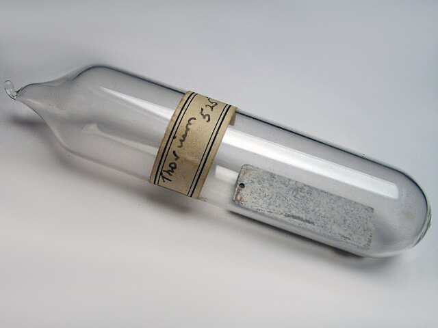 A glass bottle containing thorium metal, prominently featuring a labeled design for identification.
