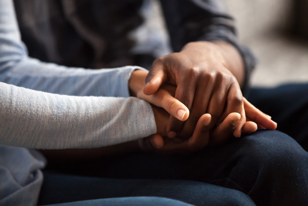 Close up black woman and man in love sitting on couch two people holding hands. Symbol sign sincere feelings, compassion, loved one, say sorry. Reliable person, trusted friend, true friendship concept

