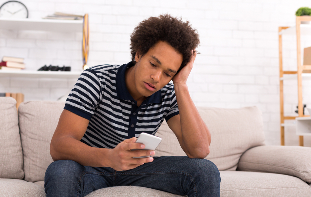 Despair teen guy reading bad news on smartphone at home, copy space
