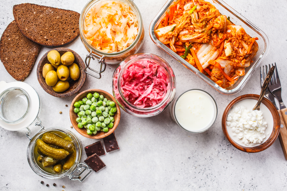 Probiotics food background. Kimchi, beet sauerkraut, sauerkraut, cottage cheese, olives, bread, chocolate, kefir and pickled cucumbers in glass jars, white background, top view.
