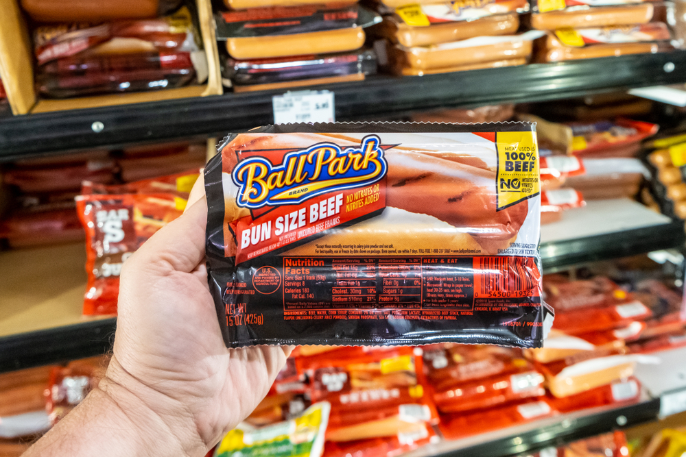 Los Angeles, CA/USA 08/03/2019 Shoppers hand holding a plastic package of Ballpark brand bun size beef frank hotdog sausages in a supermarket aisle
