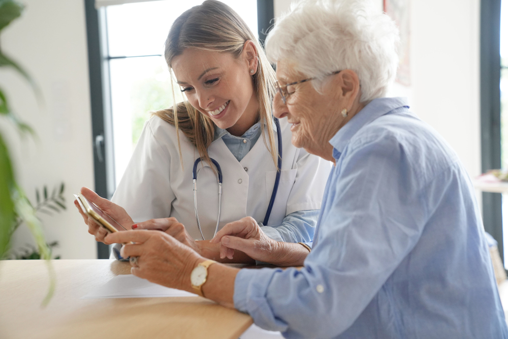 Elderly woman with nurse at home looking at tablet

