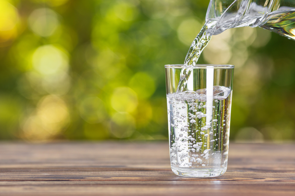 water from jug pouring into glass on wooden table outdoors
