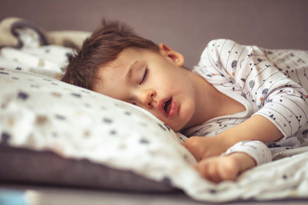 Lovely face expression with open mouth of blonde caucasian three years old child, sleeping on king bed. Sweet dreams. Little baby boy sleeping while lying on couch at home