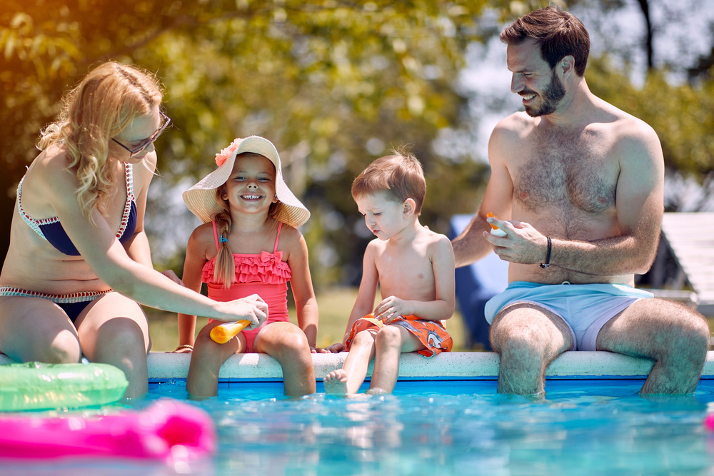 Sun protection - Family put suncream on little smiling children before swimming.
