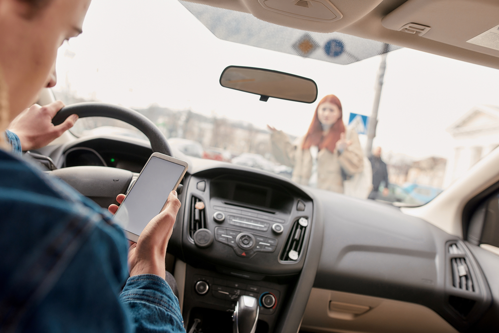 Distracted young male driver looking at the screen of his mobile phone while running over a pedestrian. Technology and transportation concept. Selective focus on hand with smartphone. Horizontal shot