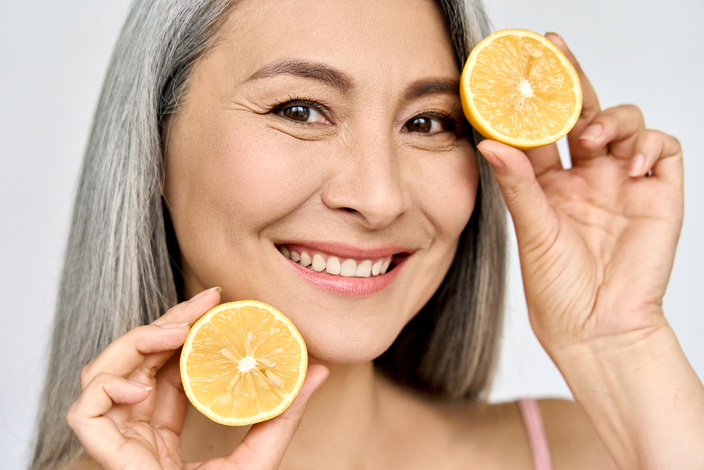 Beauty. Closeup portrait of happy smiling middle aged beautiful Asian 50s woman with perfect natural face makeup holding citrus juicy lemon. Vitamin C cosmetics skin treatment advertising concept.
