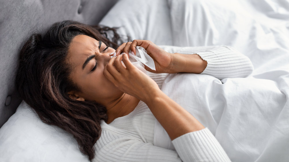 Sick black woman suffering from running stuffy nose and sore throat. Upset ill African American lady lying in bed, blowing her nose using paper napkin tissue, banner. Cold And Flu Concept